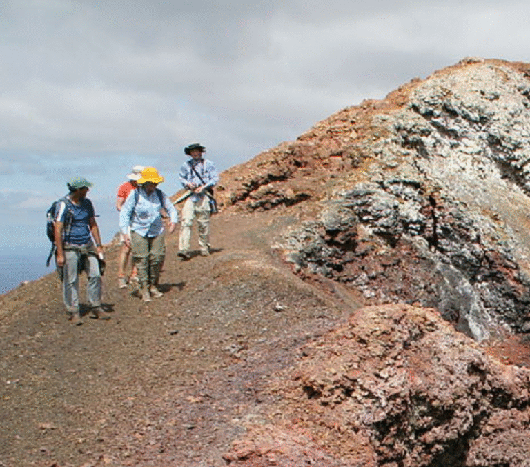 Group of hikers walking along a rocky volcanic trail with colorful hats and backpacks on a ridge.