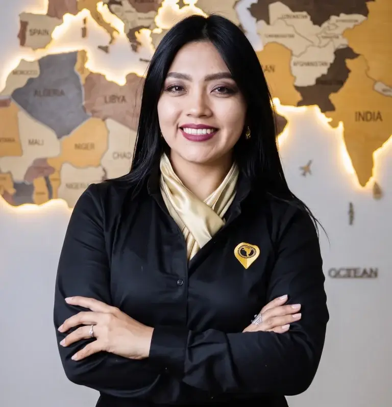 Woman in a black blazer and beige scarf with arms crossed, standing before a world map backdrop.