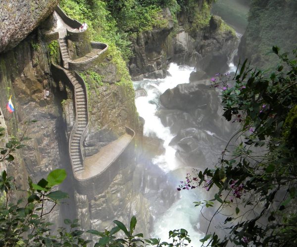 Winding stone staircase along a steep rocky gorge beside a rushing river, with lush vegetation and a few hikers.
